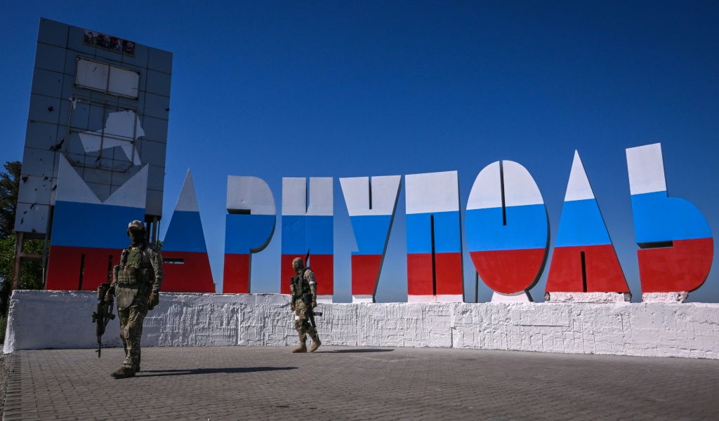 جنود روس يقومون بدوريات بجوار لافتة ترحب بالناس في مدينة ماريوبول المحتلة جنوب شرق البلاد، والتي تم رسمها بألوان العلم الروسي(ا ف ب)