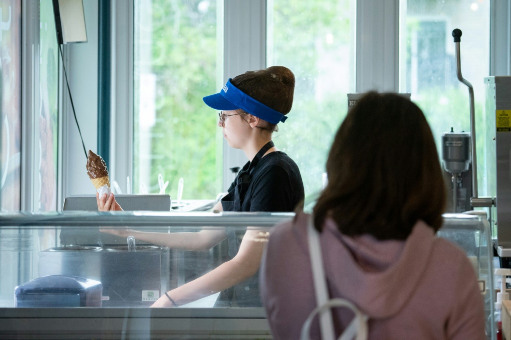 صوفيا روز آدامز ، 13 عامًا ، تغمس مخروطًا في الشوكولاتة لعميل ينتظر في المقهى وصالون الآيس كريم حيث تعمل في سانت ماتياس سور ريشيليو ، كندا (أ ف ب)