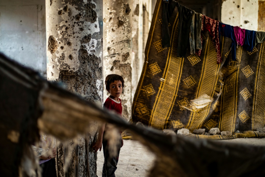 طفل سوري مهجّر من دير الزور واقفاً في مبنى متضرّر يقطن فيه مع أسرته في مدينة الرقّة في 18 حزيران/يونيو 2022 (ا ف ب).
