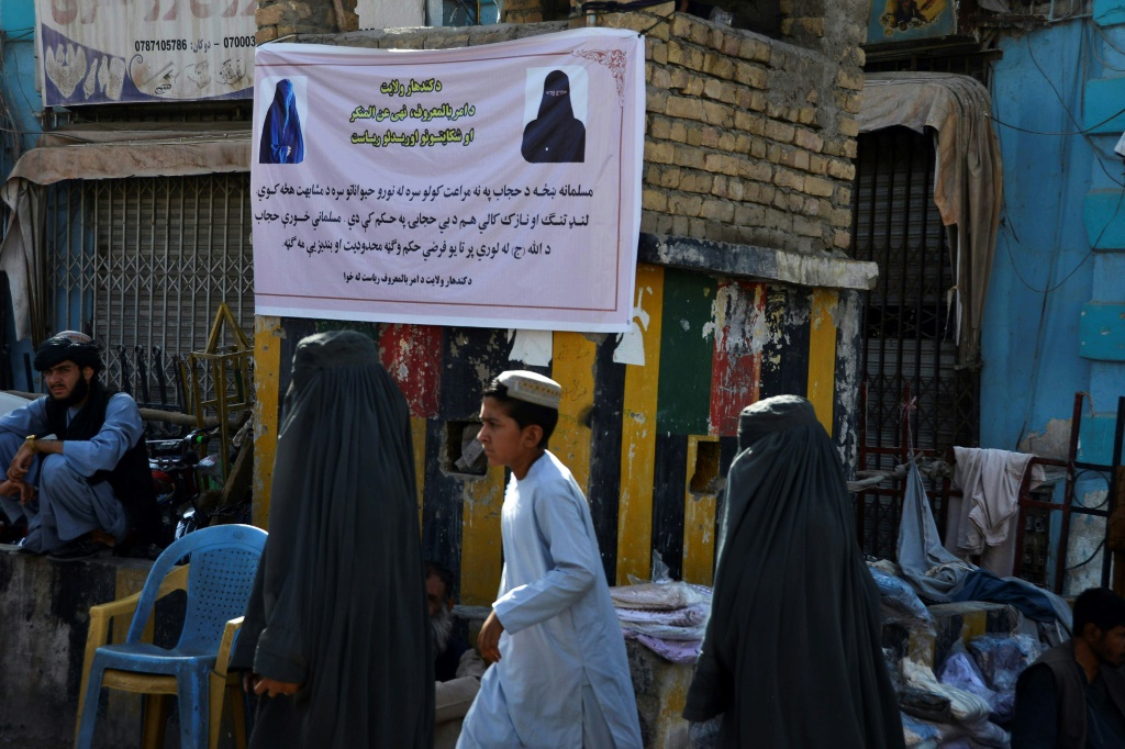نساء يرتدين البرقع يمشين أمام لافتة في قندهار تخبرهن كيف يرتدين الملابس في الأماكن العامة (ا ف ب)