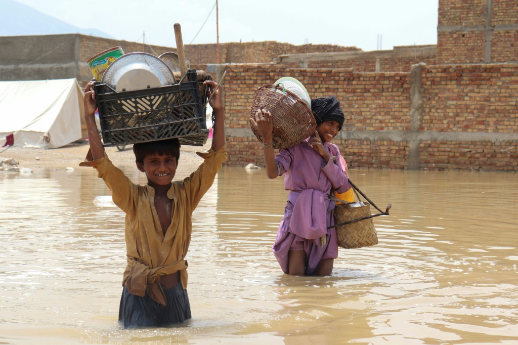  أطفال يحملون الأدوات المنزلية عبر منطقة غمرتها المياه بالقرب من كويتا في باكستان خلال الأمطار الموسمية (ا ف ب)
