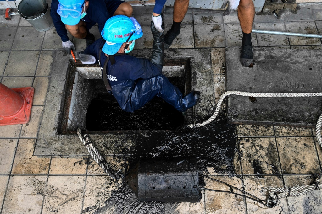 صورة ملتقطة في 21 حزيران/يونيو 2022 تظهر سجناء متطوعين يسحبون نزيلا آخر من داخل قناة للصرف الصحي بعد تنظيفها في منطقة دين داينغ في العاصمة التايلاندية بانكوك (ا ف ب)