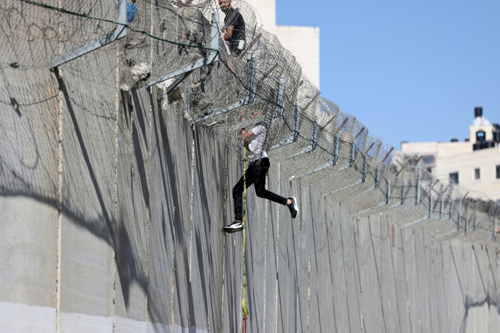 شاب فلسطيني ينحدر على حبل فوق الجدار الإسرائيلي الفاصل في القدس الشرقية بعد عبوره من بلدة الرام في 11 تموز/يوليو 2022 (أ ف ب)
