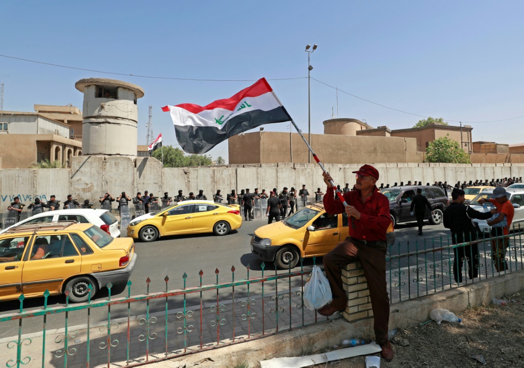 متظاهر يلوح بالعلم العراقي بينما قوات الأمن تحرس المنطقة خارج مكتب التأشيرات التركية في بغداد في 21 تموز/يوليو 2022 خلال تظاهرة احتجاج على هجوم قتل خلاله مدنيون في إقليم كردستان ونُسب إلى القوات التركية(اف ب)