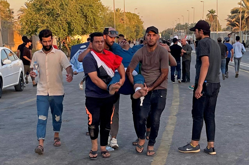 أنصار رجل الدين الشيعي العراقي مقتدى الصدر يحملون رجلا مصابا خلال احتجاج خارج المنطقة الخضراء ببغداد يوم الأربعاء (ا ف ب)