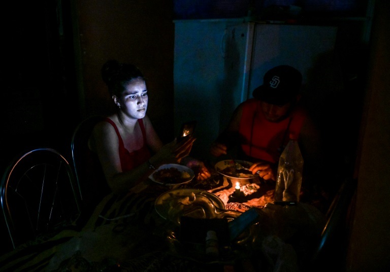 صورة التُقطت في 25 أيار/مايو 2022 تُظهر امرأة تنظر إلى هاتفها الجوّال على مائدة طعام مع رجل، وهما يجلسان على ضوء الشمعة خلال انقطاع للتيار الكهربائي في هافانا عاصمة كوبا (ا ف ب)