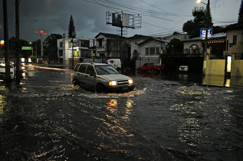  سيارة تسير على طريق تفيض فيه المياه في سان سلفادور في 16 تموز/يوليو 2022 (ا ف ب)