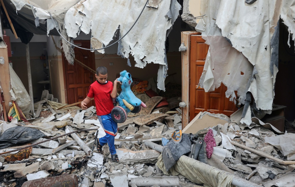 طفل فلسطيني يحمل لعبة انتُشلت من بين أنقاض منزله الذي دُمّر خلال الأعمال العدائية بين الجهاد الإسلامي وإسرائيل، في 8 آب/أغسطس 2022 في رفح جنوب قطاع غزة (أ ف ب)   