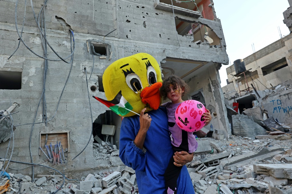 فلسطيني بزي مهرج يحمل طفلة في رفح وسط أنقاض منزل دمر في جولة العنف الأخيرة في قطاع غزة، في 9 آب/أغسطس 2022 (ا ف ب)