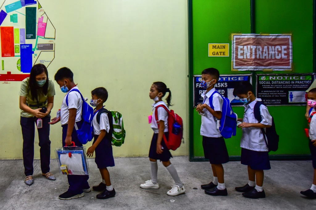 معلمة تعقم أيدي التلاميذ في اليوم الأول من إعادة فتح المدارس بعد إغلاق استمرّ عامين، في مدرسة ابتدائية في مانيلا في 22 آب/أغسطس 2022 (ا ف ب)