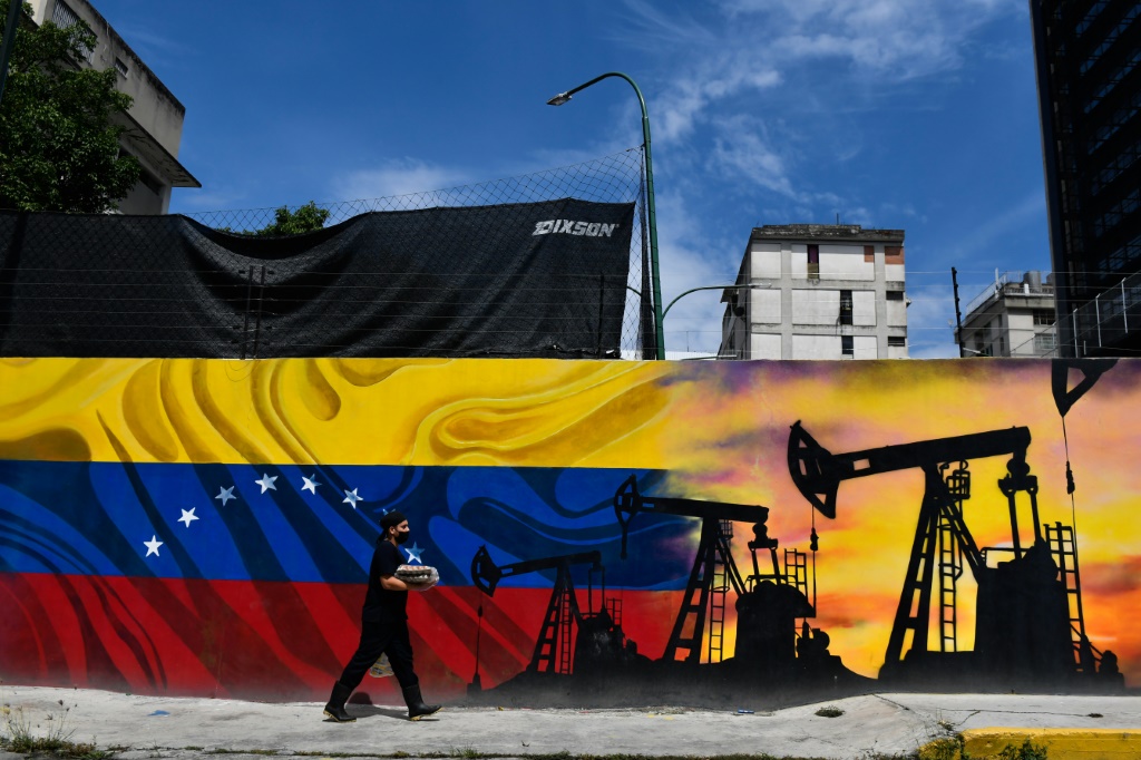 رجل يمر أمام جدارية تمثل مضخة نفط وعلم فنزويلا في احد شوارع كراكاس في 26 أيار/مايو 2022. (ا ف ب)