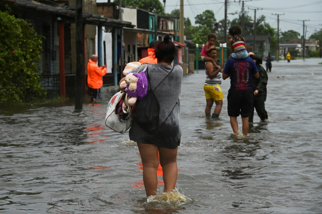 أناس يسيرون في مدينة باتابانو الكوبية في شارع غمرته مياه فيضانات ناجمة عن مرور الإعصار إيان في 27 أيلول/سبتمبر 2022 (ا ف ب)