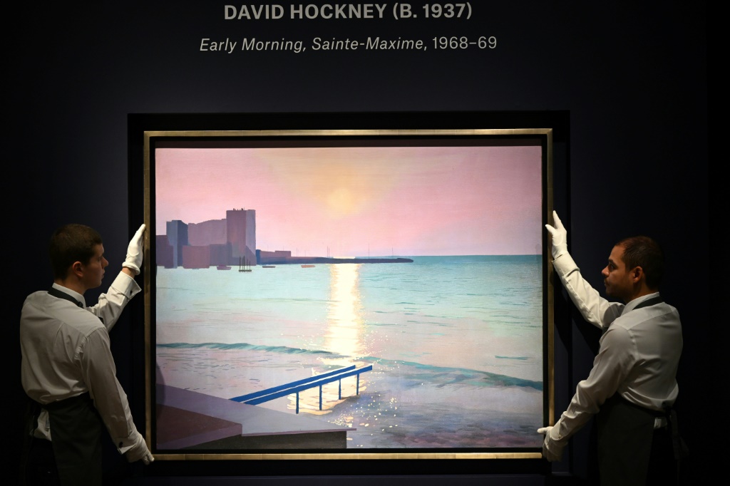 صورة التقطت في 6 تشرين الأول/أكتوبر 2022 لعاملين يحملان لوحة "إيرلي مورنيننغ، سانت ماكسيم" للرسام البريطاني ديفيد هوكني في دار "كريستيز" في لندن (ا ف ب)