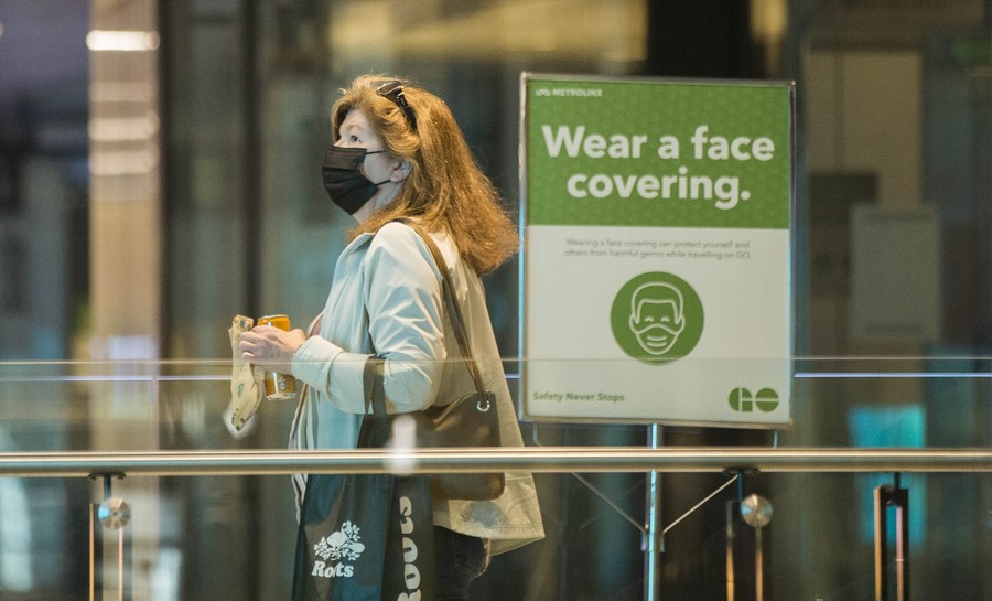 امرأة ترتدي الكمامة تمر أمام إشعار يذكر الناس بارتداء الكمامة في محطة الاتحاد في تورنتو، كندا، في 11 مايو 2022. (شينخوا)