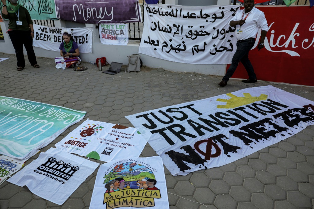 ناشط مناخي يجلس إلى جانب لافتات موضوعة على الأرض تطالب بحماية حقوق الإنسان والتعويض على أضرار التغير المناخي في شرم الشيخ في مصر في 18 تشرين الثاني/نوفمبر (ا ف ب)