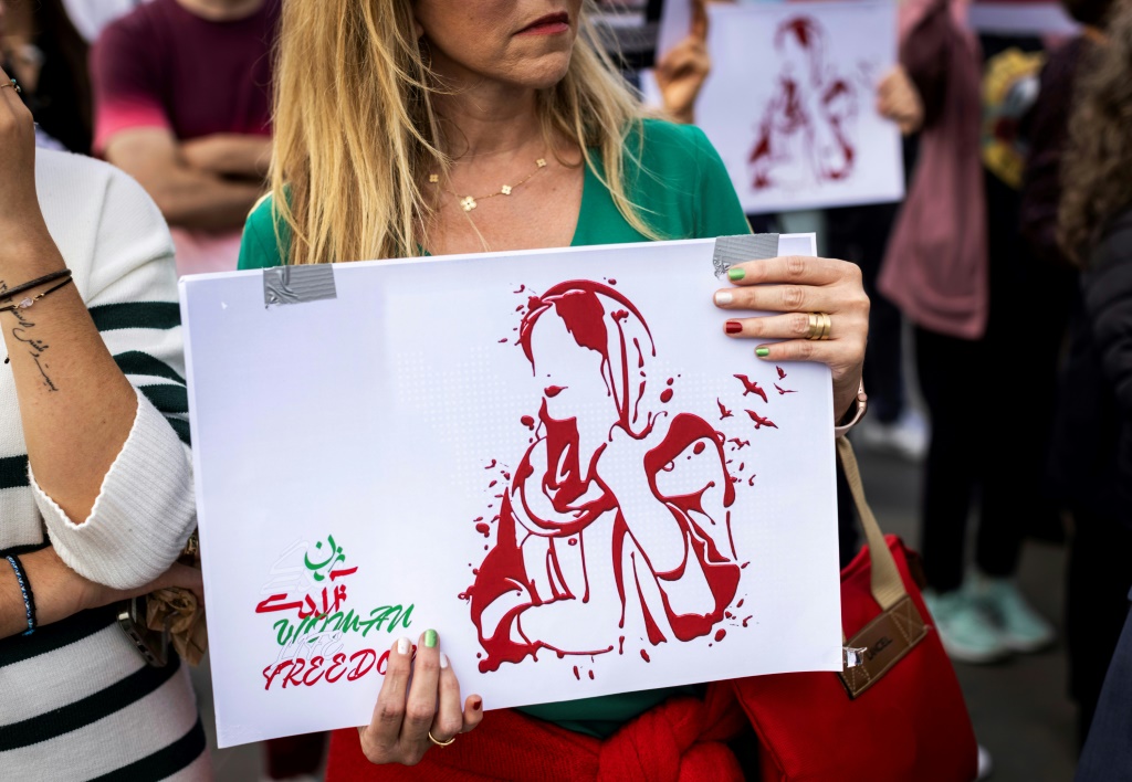 امرأة تحمل صورة الشابة الإيرانية مهسا أميني خلال مسيرة لدعم المحتجّين في إيران، في ساحة الجمهورية في باريس، في 29 أكتوبر/تشرين الأول 2022 (ا ف ب)