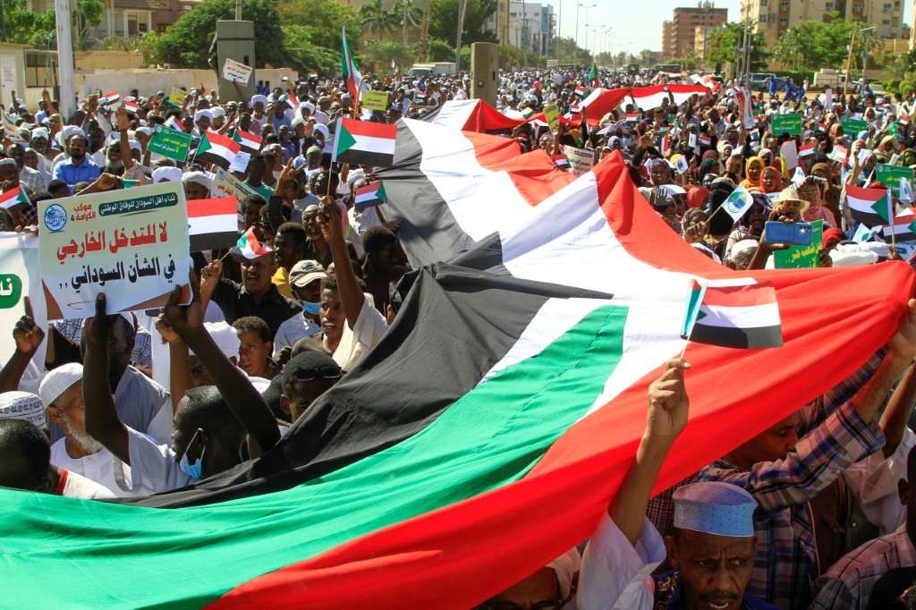  متظاهرون سودانيون يرفعون علمًا وطنيًا عملاقًا أثناء مسيرة أمام مقر الأمم المتحدة في الخرطوم في 3 ديسمبر / كانون الأول (أ ف ب)