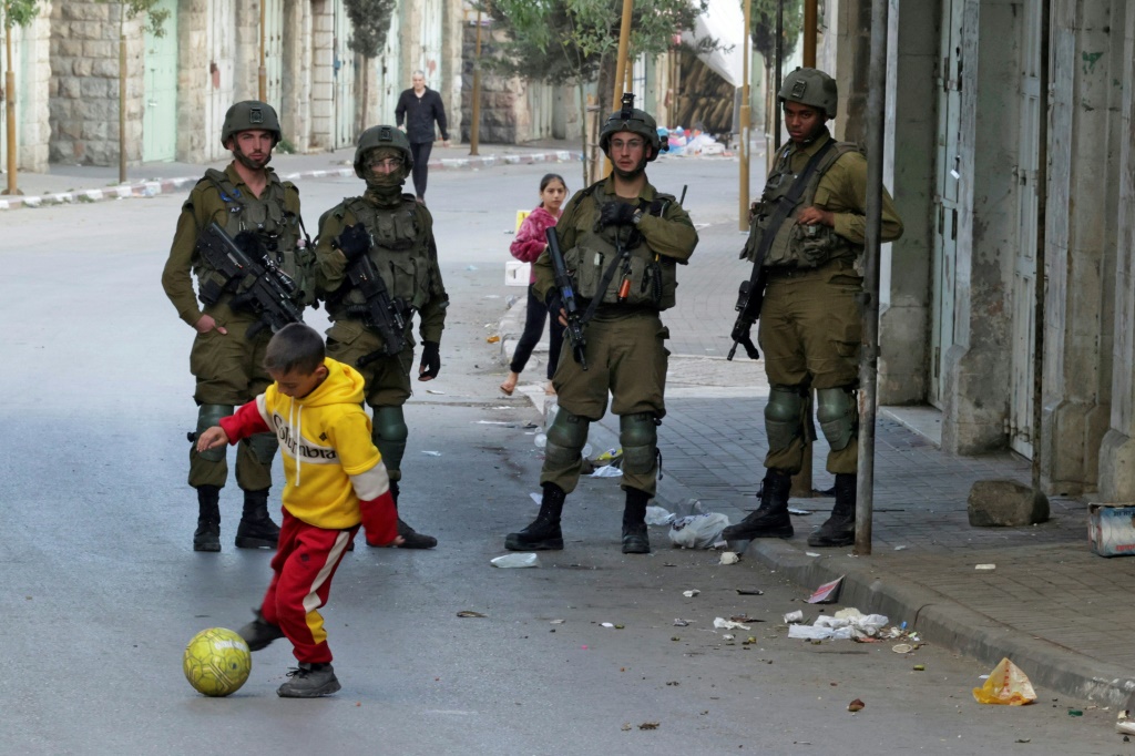 طفل فلسطيني يلعب كرة القدم في الشارع المجاور لقوات الأمن الإسرائيلية في دورية وسط مدينة الخليل بالضفة الغربية المحتلة ، 18 نوفمبر 2022 (أ ف ب)