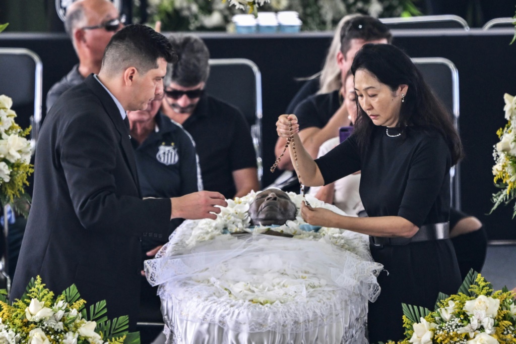 زوجة أسطورة كرة القدم البرازيلي الراحل بيليه، مارسيا أوكي (يمين)، الى جانب نعشه أثناء مراسم الجنازة المفتوحة في سانتوس. (ا ف ب)
