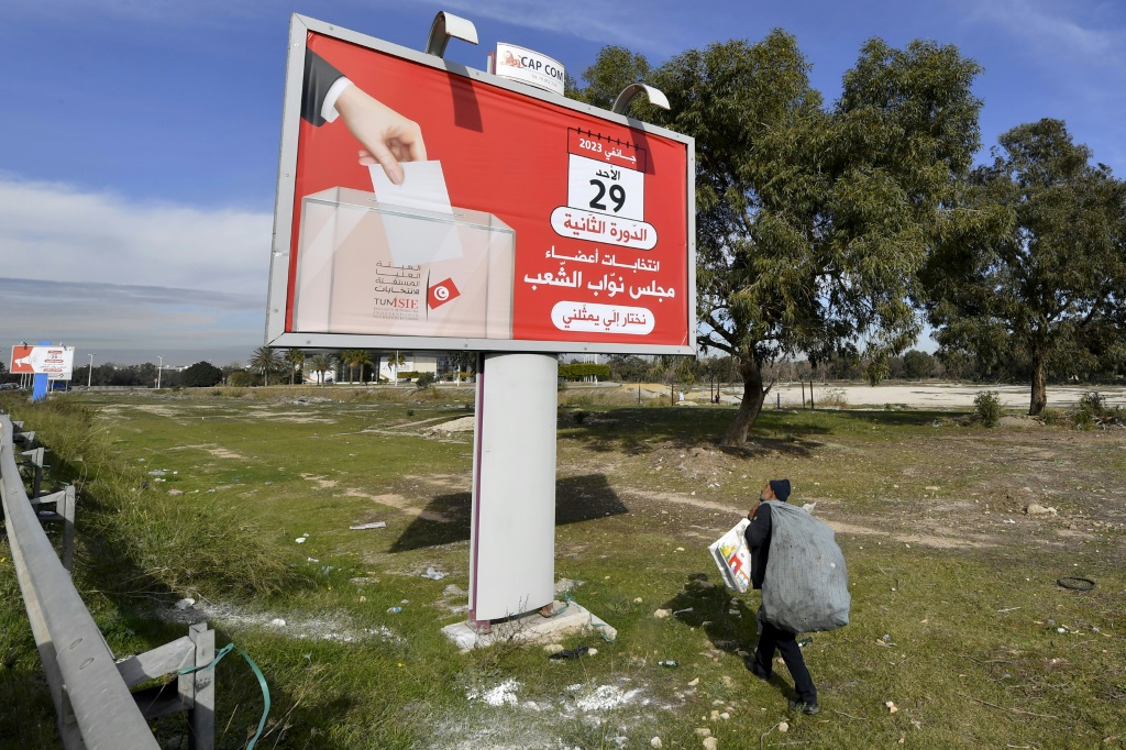    نابش قمامة يمر قرب لافتة للحملة الانتخابية النيابية في تونس في 25 كانون الثاني/يناير 2023. (ا ف ب)