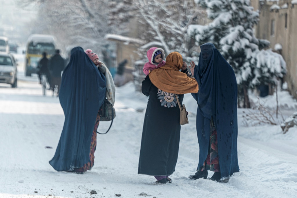 أفغانيات يحملن أطفالا يمشين في شارع مكسو بالثلج في كابول في 23 كانون الثاني/يناير 2023 (ا ف ب)