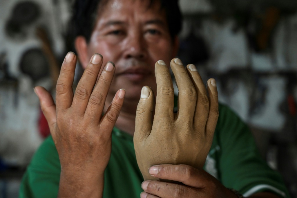علي ساغا يعرض يداً اصطناعية (يمين) مقارناً اياها بيده، داخل مشغله في تانغيرانغ الاندونيسية بتاريخ 18 كانون الثاني/يناير 2023 (ا ف ب)