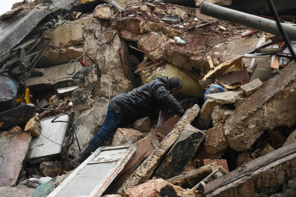 رجل يبحث عن ناجين بين أنقاض مبنى منهار في حلب في منطثة سيطرة النظام السوري بعد زلزال قوته 7,8 درجات ضرب تركيا وسوريا في السادس من شباط/فبراير 2023 (ا ف ب)