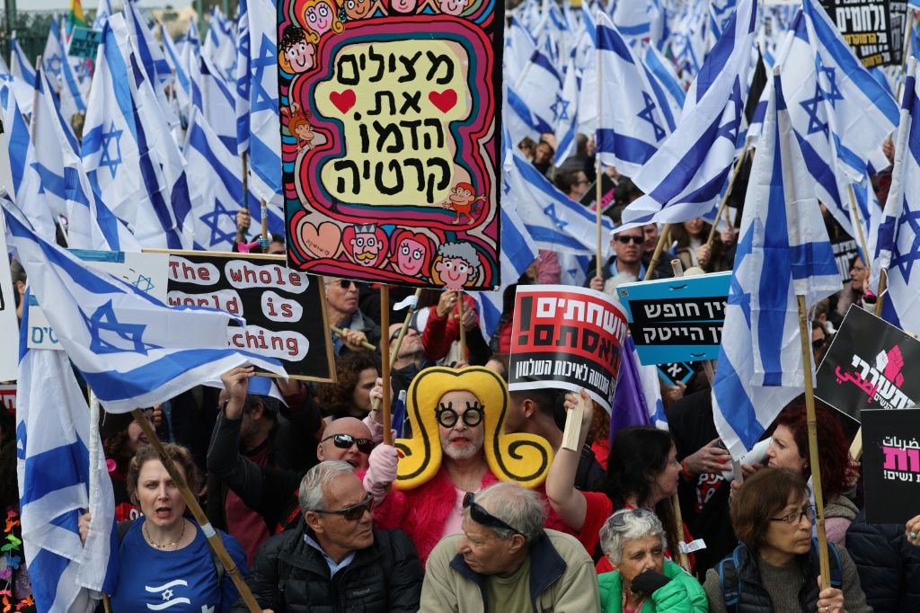     متظاهرون إسرائيليون يلوحون بالعلم الإسرائيلي ولافتات خط عليها شعارات ضد مفترحات تعديل النظام القضائي في إسرائيل وذلك أمام البرلمان الإسرائيلي (الكنيست) في 13 شباط/فبراير 2023 (أ ف ب)