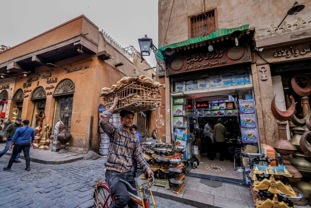 صورة التقطت في 27 شباط/فبراير 2023 لعامل توصيل يحمل أرغف خبز على رأسه وهو يركب دراجة في شارع في القاهرة القديمة (أ ف ب)   