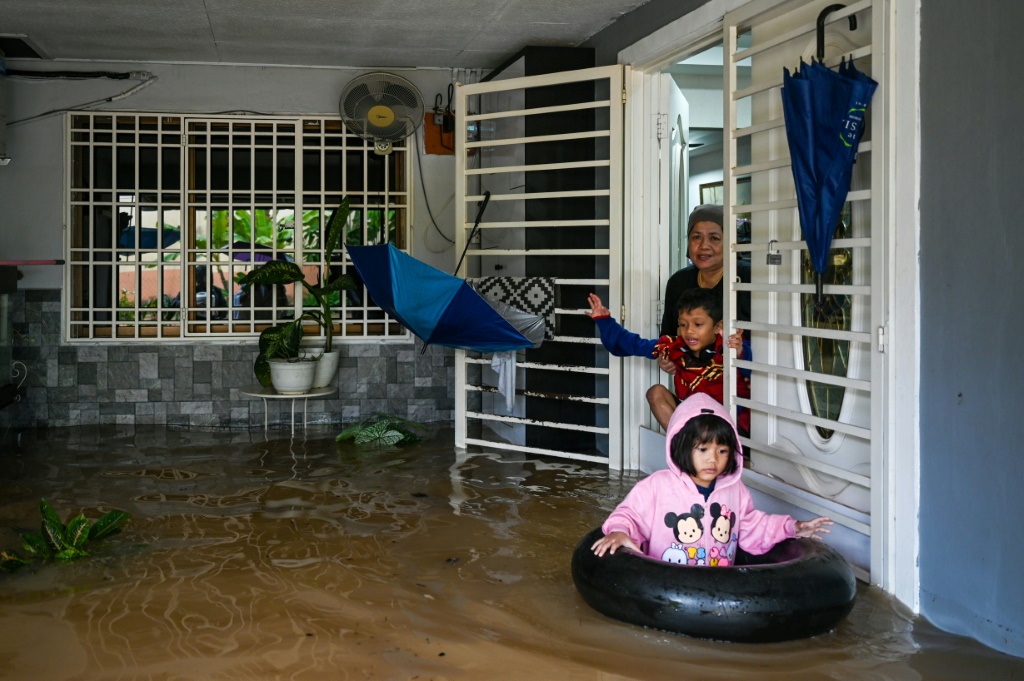 امرأة وأطفالها يستعدون لإخلاء منزلهم في منطقة غمرتها المياه في يونغ بينغ بولاية جوهور الماليزية (أ ف ب)