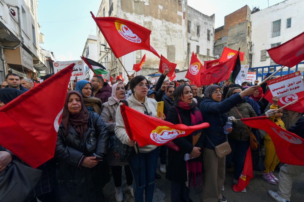    متظاهرون يرفعون لافتات وأعلام خلال مسيرة مناهضة للحكومة دعا إليها اتحاد نقابات العمال النافذ في تونس، في 4 آذار/مارس 2023. (أ ف ب)