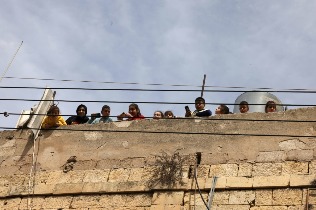 فلسطينيون يشاهدون من سطح منزلهم مستوطنين إسرائيليين يحتفلون بعيد بوريم ويسيرون في شارع الشهداء، المغلق إلى حد كبير أمام الفلسطينيين، في وسط مدينة الخليل في الضفة الغربية المحتلة في 7 آذار/مارس 2023 (ا ف ب)
