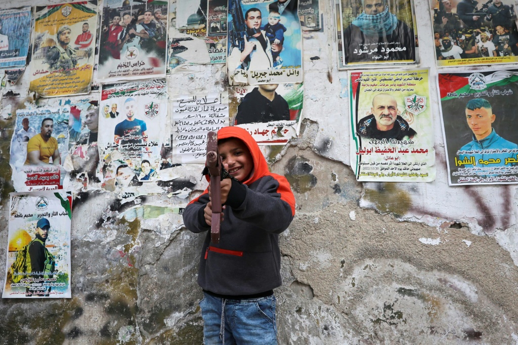 فتى فلسطيني يقف لالتقاط صورة مع لعبة مسدس خلال مسيرة لإحياء الذكرى الأولى لمقتل نادر ريان البالغ من العمر 16 برصاص القوات الإسرائيلية، في مخيم بلاطة للاجئين في الضفة الغربية المحتلة، في 17 آذار/مارس، 2023 (ا ف ب)