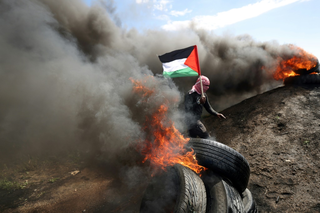    متظاهر فلسطيني يحمل العلم فيما يقوم آخرون باحراق اطارات في غزة خلال تظاهرة احتجاج على لقاء مصر في 19 آذار/مارس 2023. (ا ف ب)