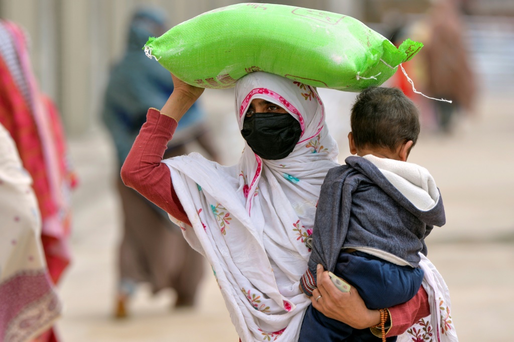     سيدة تحمل طفلها وكيس دقيق من نقطة توزيع في العاصمة الباكستانية (أ ف ب)