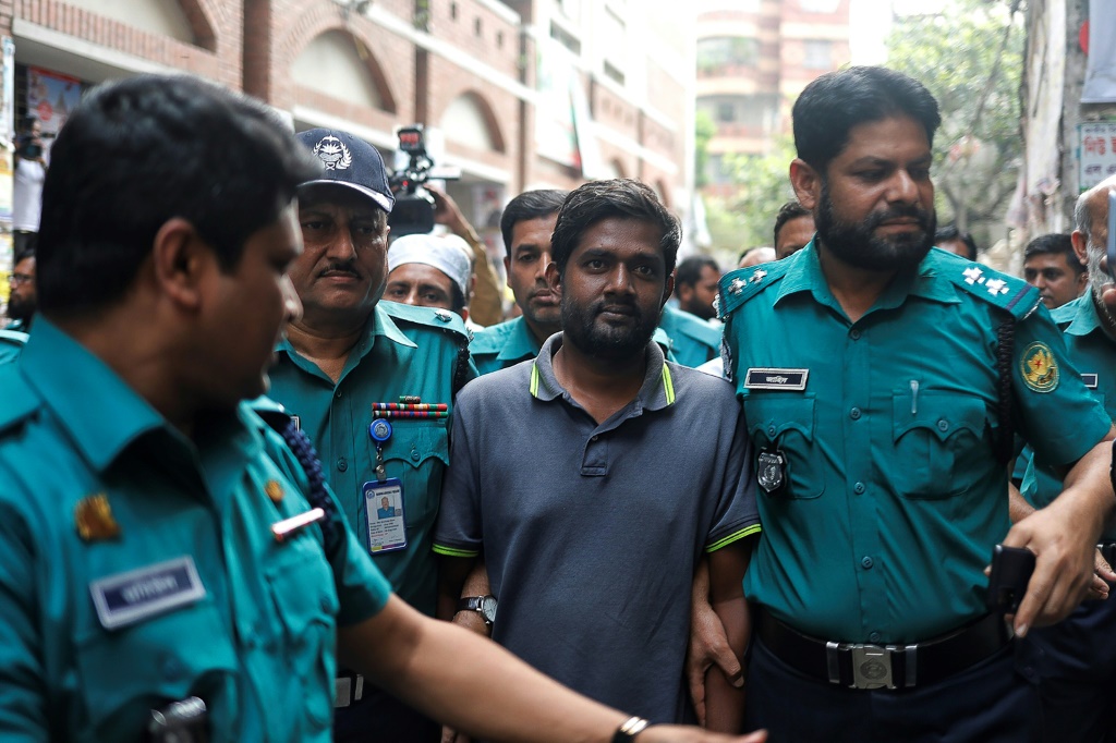    مرافقة مراسل الشرطة شمس الزمان شمس (وسط) ، الذي تم القبض عليه واتهامه بموجب قانون الأمن الرقمي ، أمام محكمة في دكا. (ا ف ب)   