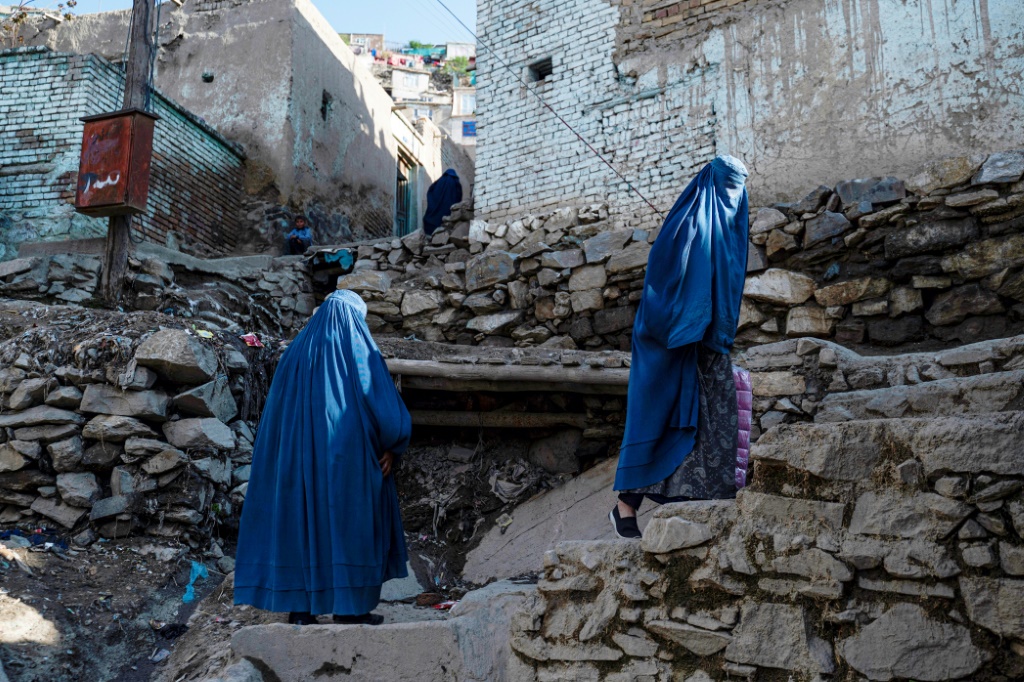 نساء أفغانيات يرتدين البرقع يتسلقن ممرًا صخريًا إلى منازلهن في منطقة شور بازار بالعاصمة (أ ف ب)