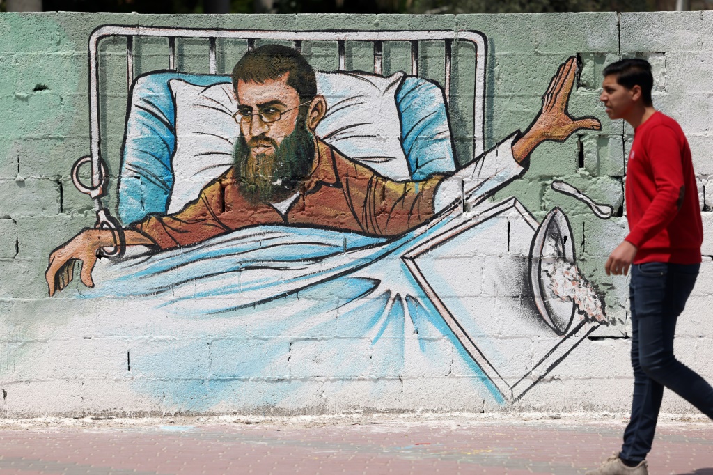     فلسطيني يمشي أمام لوحة جدارية في غزة يظهر فيها خضر عدنان ، أحد قياديي حركة الجهاد الإسلامي ، الذي يضرب عن الطعام منذ أكثر من 80 يومًا احتجاجًا على اعتقاله دون توجيه اتهامات إليه في أحد السجون الإسرائيلية (أ ف ب)   