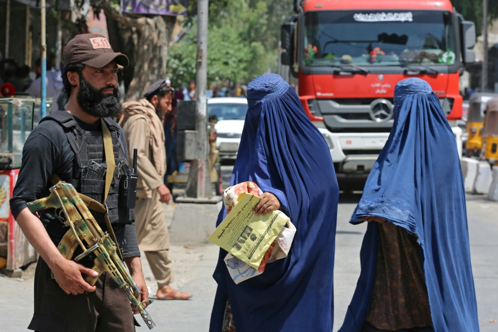 امرأتان أفغانيتان ترتديان البرقع تمران قرب عنصر أمن من حركة طالبان في جلال آباد في أفغانستان في 30 نيسان/أبريل 2023 (أ ف ب)