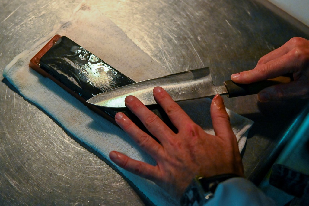 طاه يشحذ سكينا بحجر في مطبخ مطعمه في طوكيو في 18 تشرين الثاني/نوفمبر 2022 (ا ف ب)