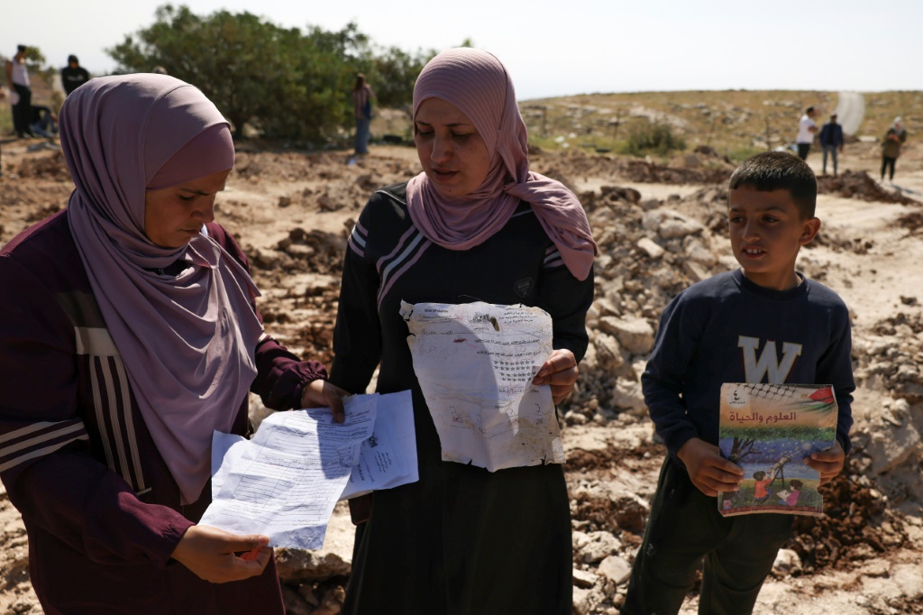 فلسطينيات يجمعن اوراقا وكتب من موقع مدرسة التحدي خمسة التي هدمتها الجرافات الإسرائيلي فجر الأحد 7 أيار/مايو 2023 في قرية جب الذيب شرق بيت لحم بسبب البناء دون ترخيص (أ ف ب)