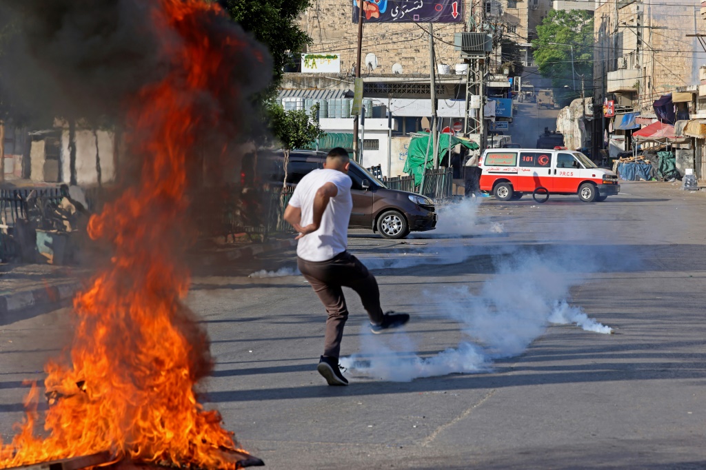 فلسطيني يركل قنبلة غاز مسيل للدموع أثناء مداهمة لمدينة نابلس في شمال الضفة الغربية المحتلة في 14 أيار/مايو 2023 (ا ف ب)
