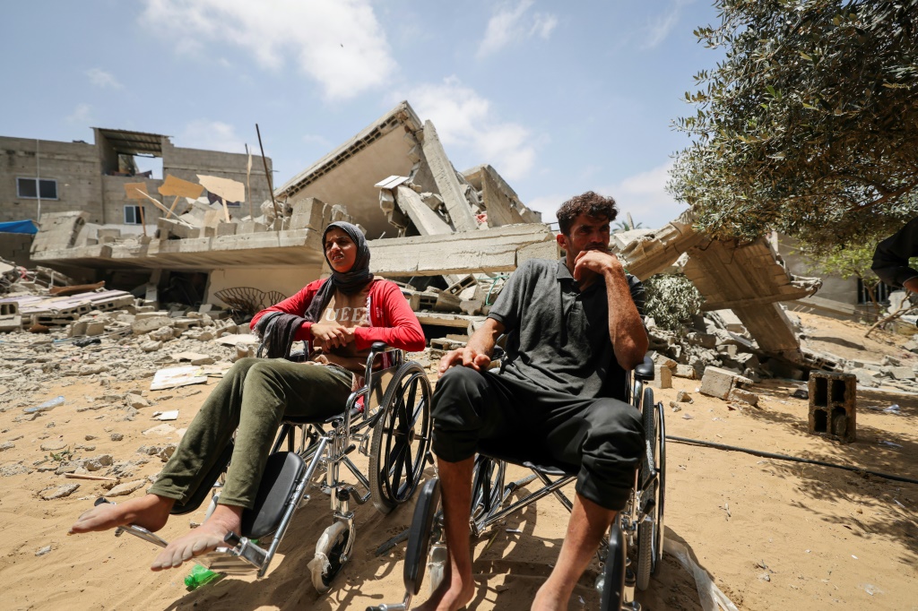 أفراد من عائلة نبهان الفلسطينية يجلسون على كراسي متحركة قرب أنقاض منزلهم بالأرض في غارة جوية إسرائيلية على بيت لاهيا شمال قطاع غزة (أ ف ب)