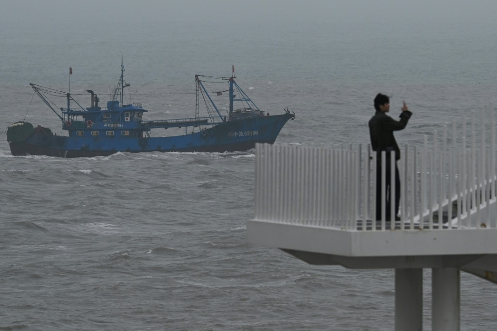 سفينة صيد تمر في مضيق تايوان فيما سائح يلتقط صورة من جزيرة بينغتان في جنوب شرق الصين في السادس من نيسان/أبريل 2023 (ا ف ب)