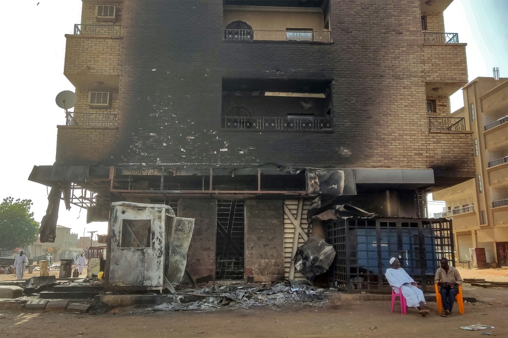     رجلان يجلسان خارج فرع بنك احترق في جنوب الخرطوم في 24 مايو 2023 (أ ف ب)