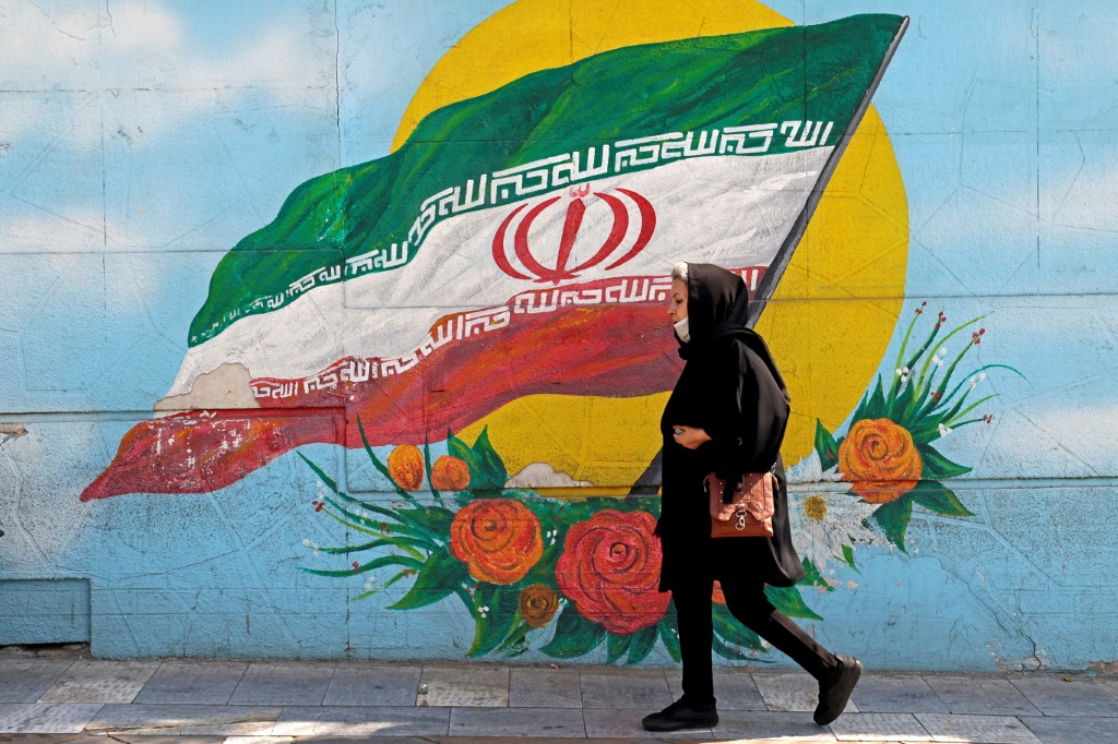 امرأة إيرانية تمشي قرب جدار مرسوم عليه علم إيراني في طهران في 10 نيسان/أبريل 2023 (ا ف ب)