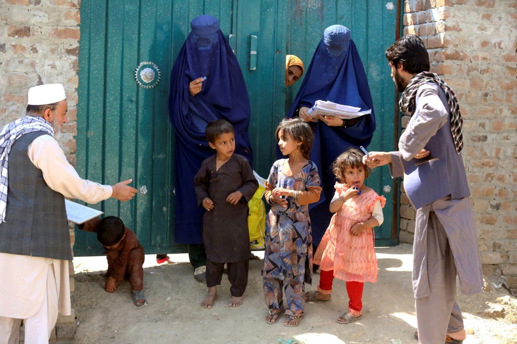    أفغانيتان تعملان في المجال الصحي أمام باب منزل خلال حملة تطعيم ضد شلل الأطفال في جلال أباد في 15 أيار/مايو 2023 (أ ف ب)