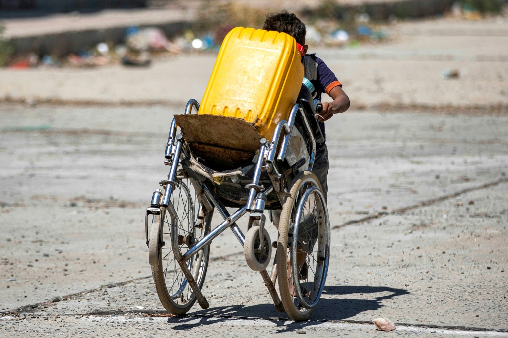 فتى يدفع كرسيًا متحرًكًا وضع عليه حاوية مملوءة بالمياه على مشارف مدينة تعز في جنوب غرب اليمن في 8 حزيران/يونيو 2023 (أ ف ب)