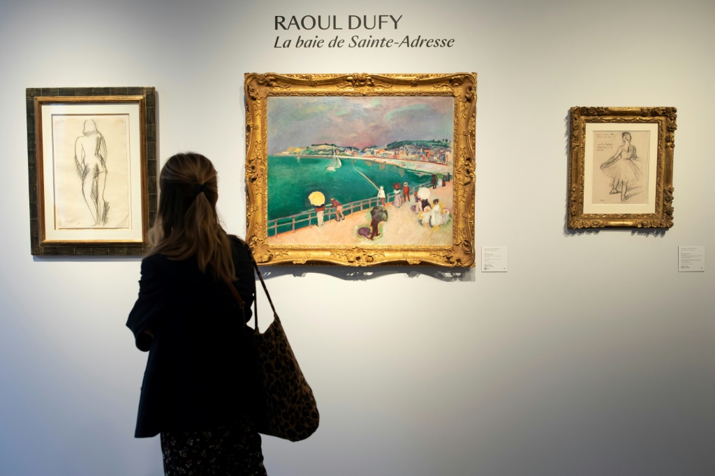 امرأة تنظر إلى لوحة زيتية لراول دوفي بعنوان "شاطئ سانت أدريس" (في الوسط) ضمن مجموعة أعمال فنية يملكها الممثل الفرنسي آلان ديلون في معرض بعنوان "60 عاما من الشغف" في دار "بونامس كورنيت دو سان سير" في باريس قبل مزاد على هذه المجموعة (ا ف ب)