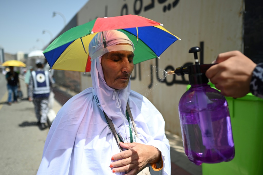 فرد أمن سعودي يرش رذاذ الماء على حاجة يبدو عليها الإنهاك في منى قرب مدينة مكة المكرمة في 29 حزيران/يونيو 2023 (ا ف ب)